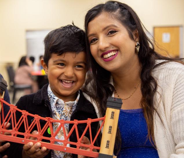 A child and his mother smile while holding a bridge toy