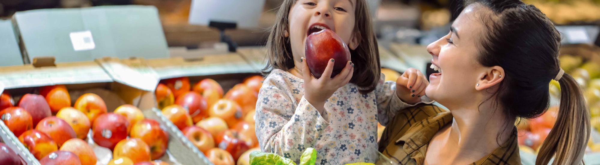 a mother and daughter smile while grocery shopping