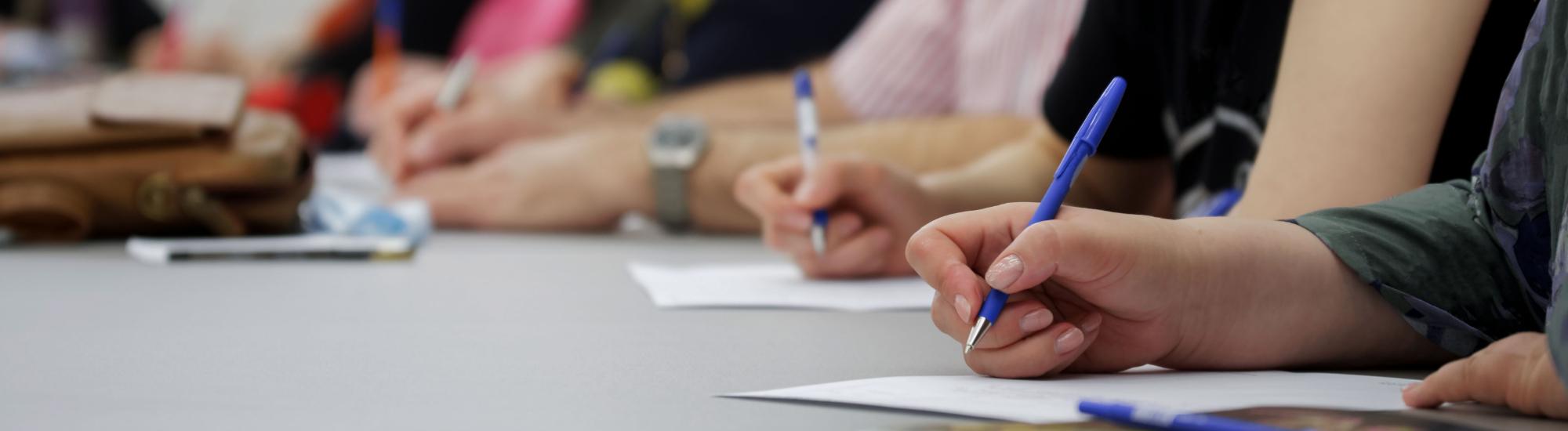 a photo of several hands  holding pens and writing on paper